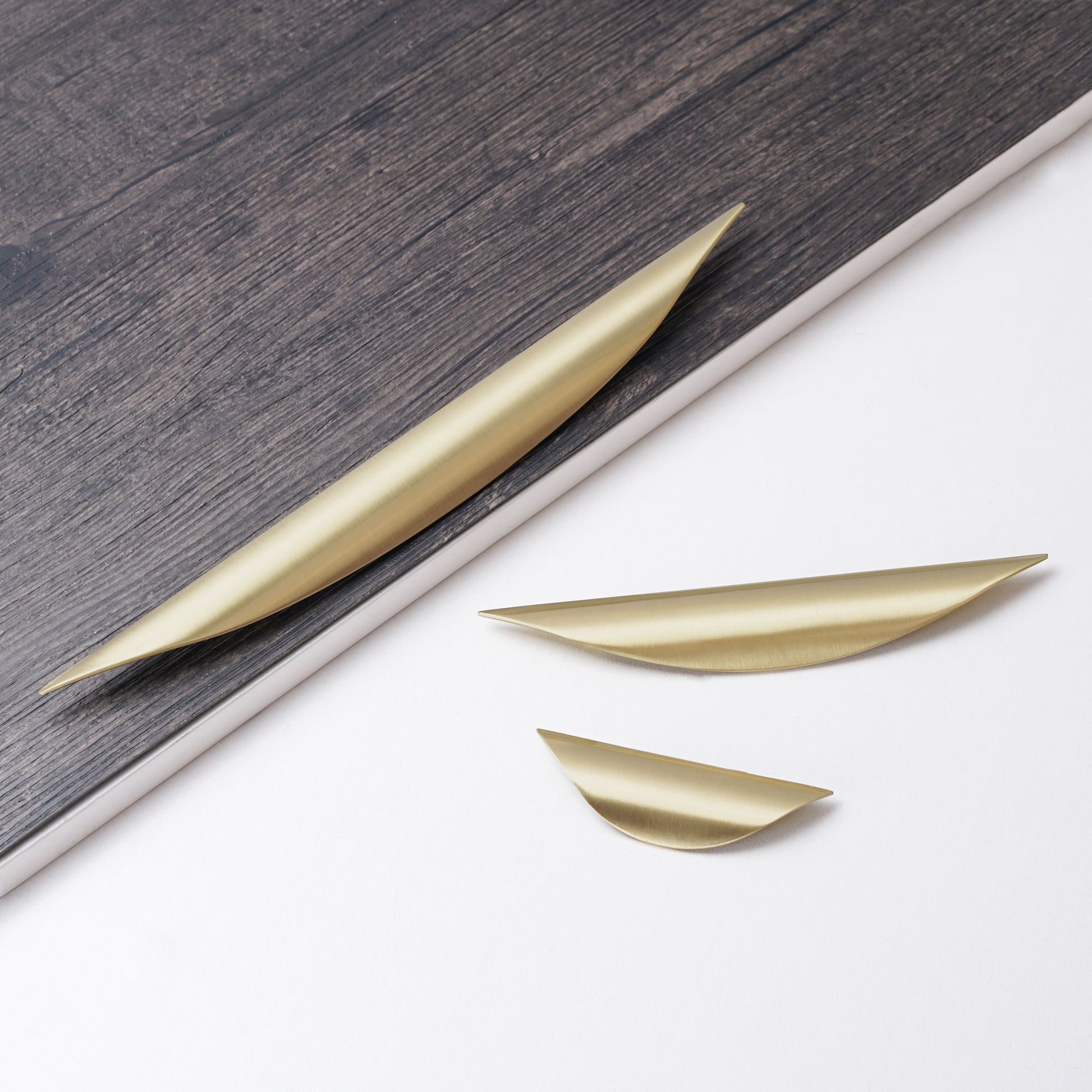 Brushed gold arc-shaped thumb handle for wooden cabinet doors.